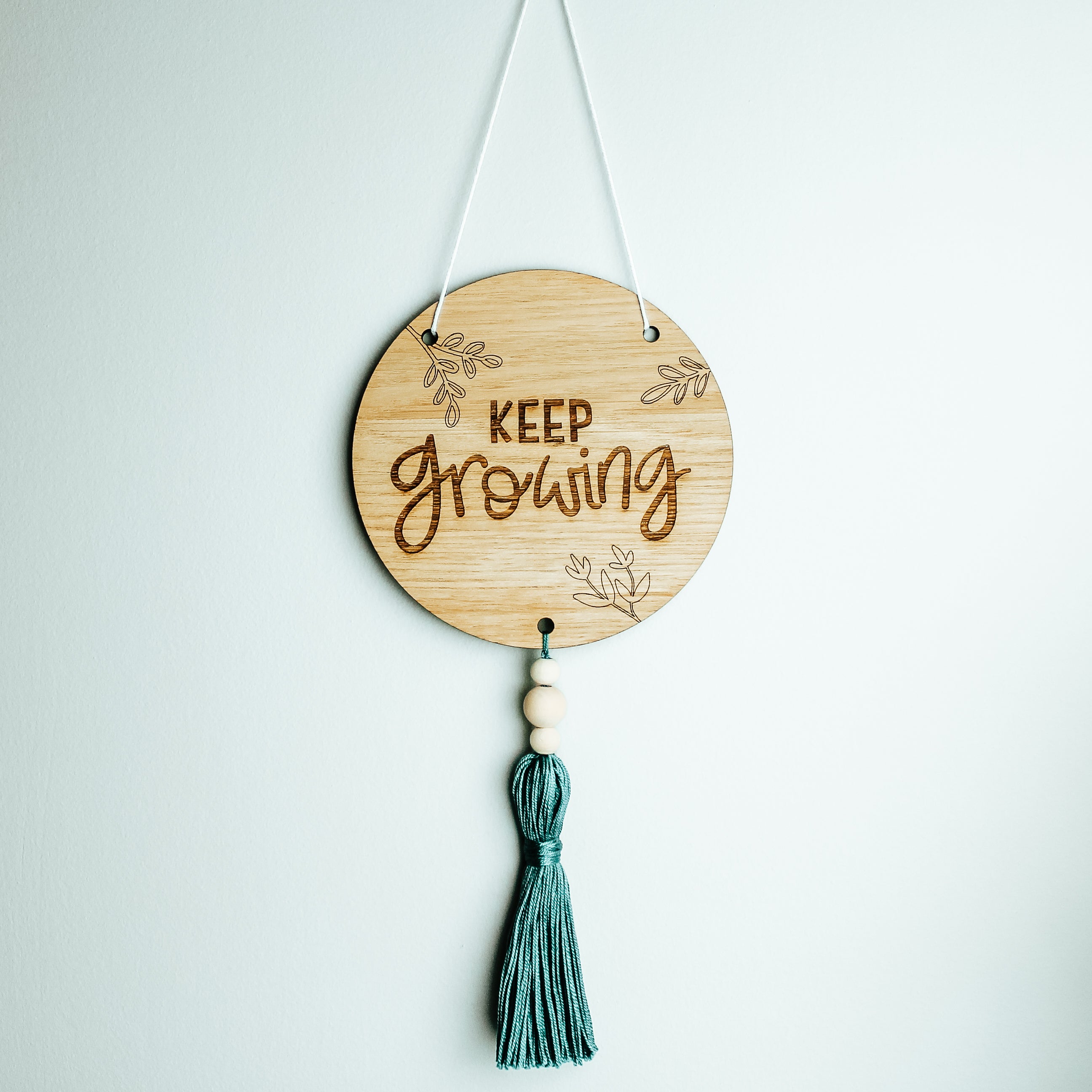 round wooden sign with tassel affixed to the bottom with the motivational phrase keep growing engraved onto it