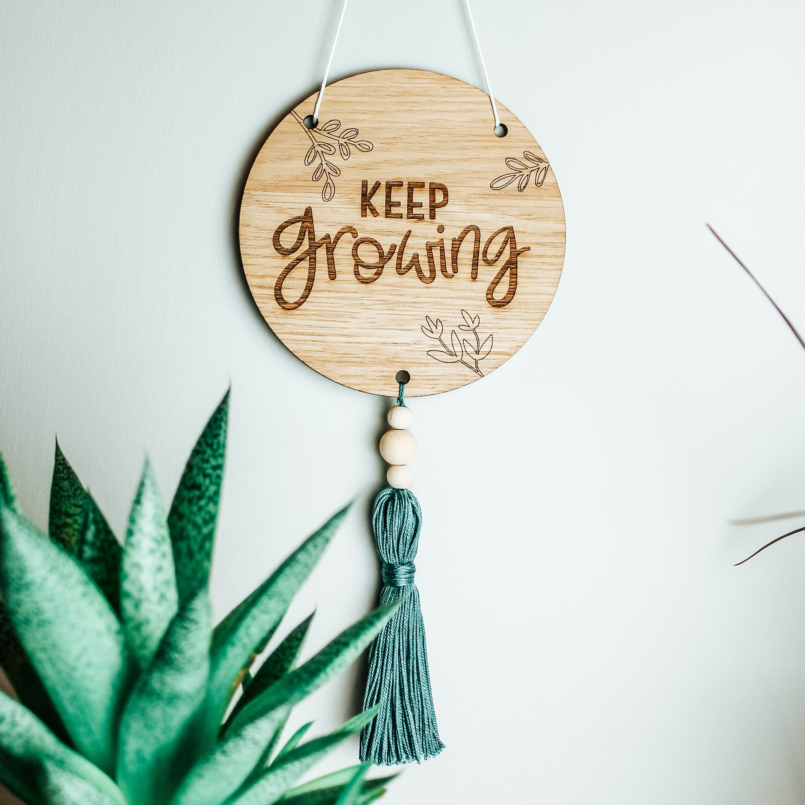 keep growing calligraphy sign engraved on a round, with a tassel affixed to the bottom. perfect for the plant lover