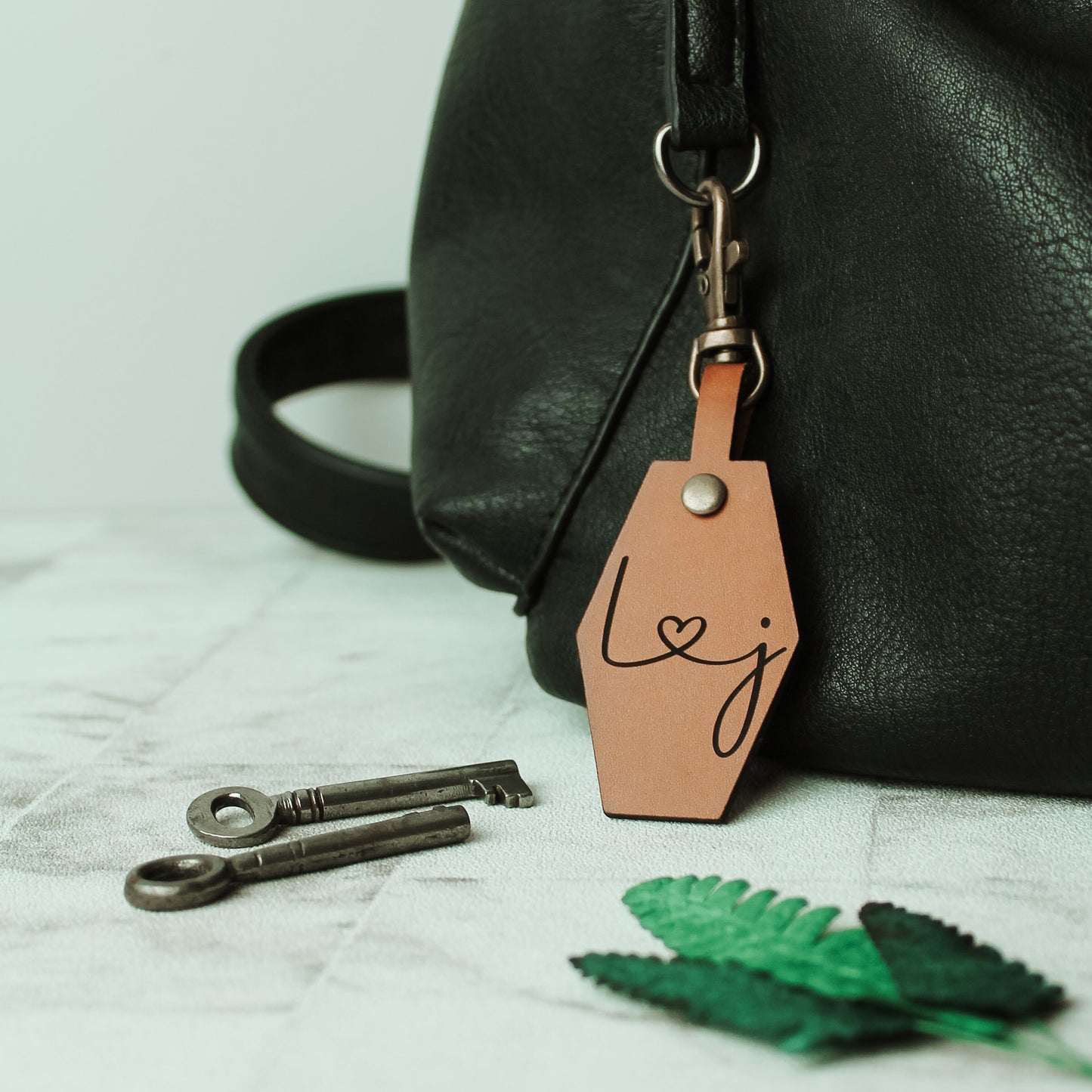 whisky coloured brown leather keyring with initials engraved on it connected by a heart design. with a swivel clasp attached to clip onto a bag