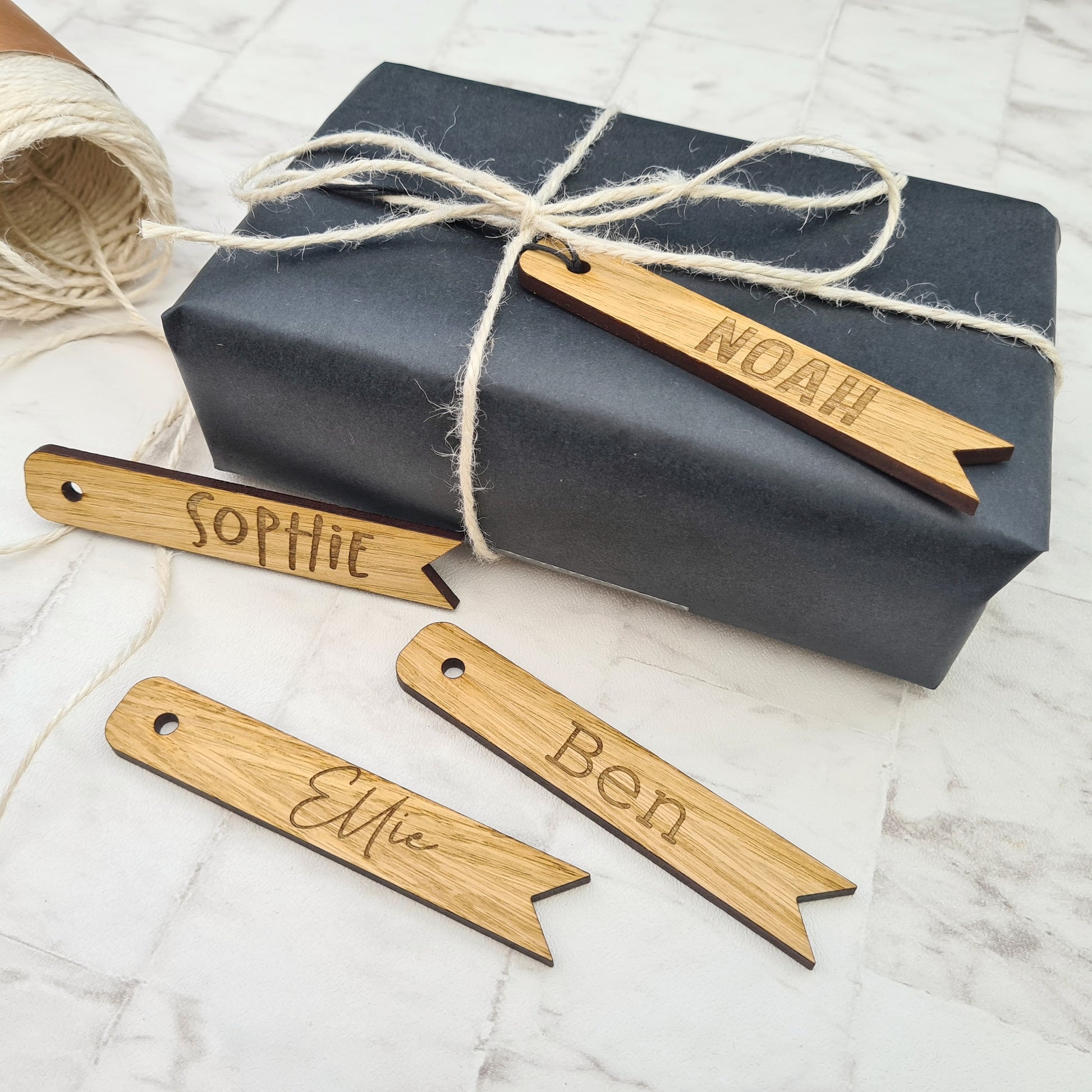 wooden personalised gift tags with names engraved onto them. Shown with a beautifully wrapped gift and some string 