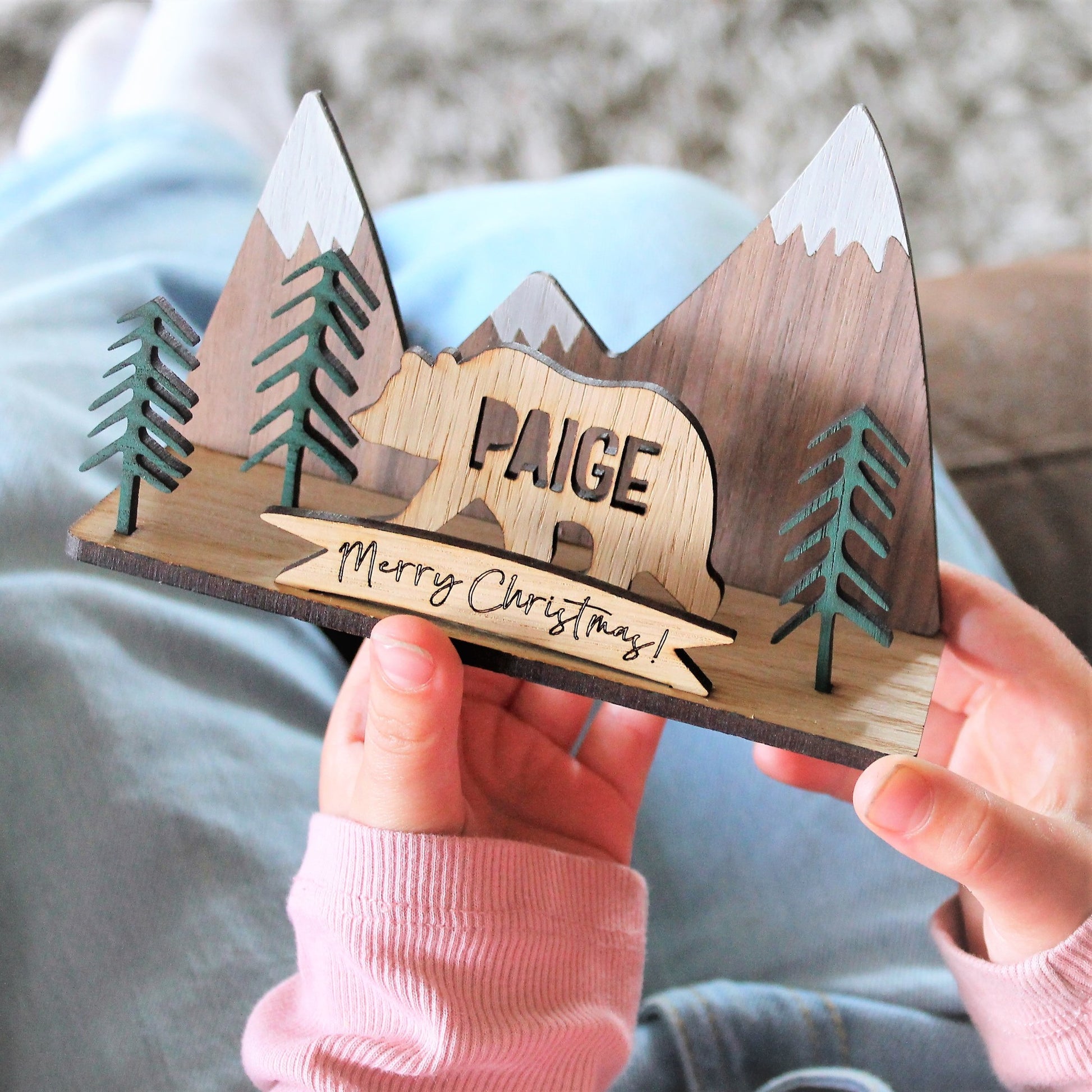 Child, putting together and playing with 3d festive wooden ornament with mountain and forest scene, and a personalised name bear