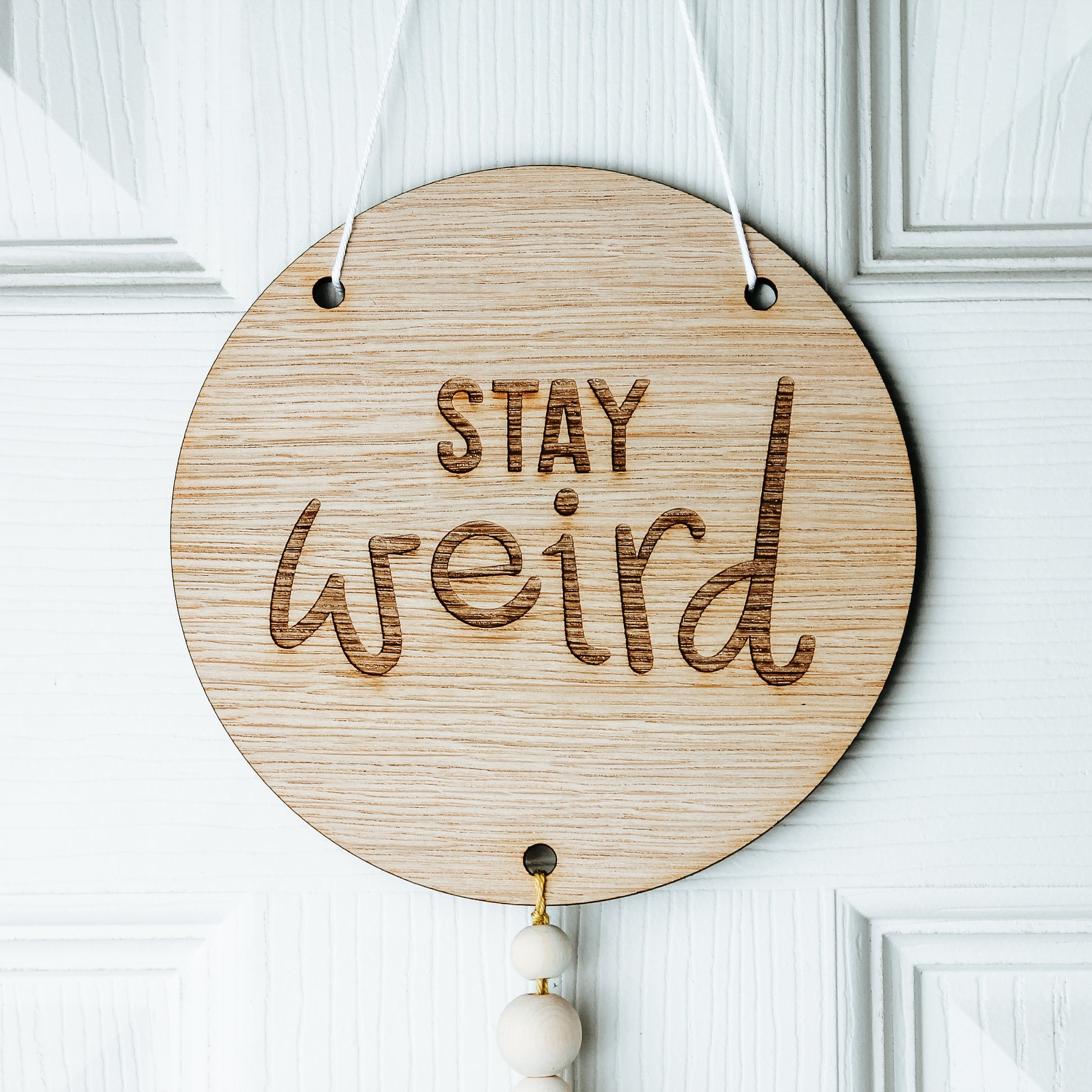 round wooden sign with stay weird engraved onto it in calligraphy writing