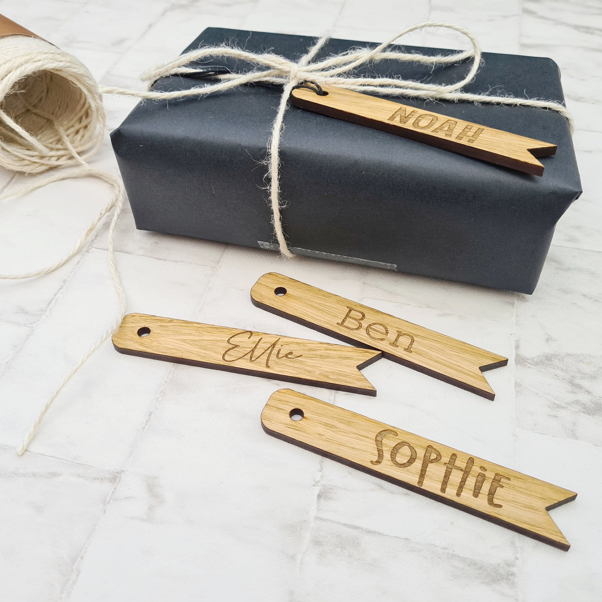 Personalised wooden gift tags, engraved with names attached to a black wrapped parcel tied up with string 