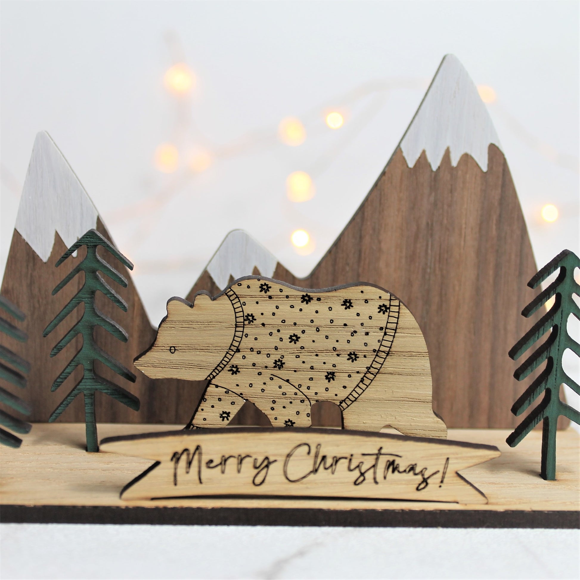 3d wooden ornament with mountain and forest scene, and a festive jumper bear